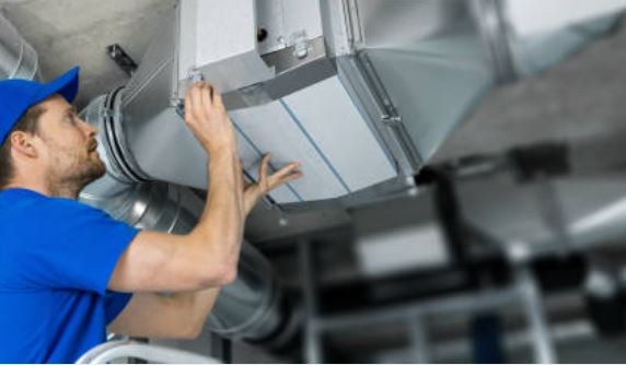 Technician reaching into a large silver duct to service it